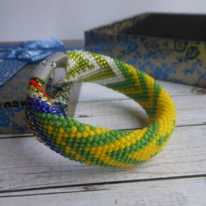 May include: A colorful beaded bracelet with a green, yellow, blue, and red pattern. The bracelet has a silver clasp.
