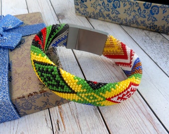 May include: A colorful beaded bracelet with a silver clasp. The bracelet is made with small beads in red, yellow, green, black, and white.