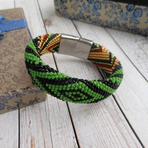 May include: A green, black, gold and red beaded bracelet with a silver magnetic clasp.