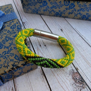 May include: A beaded bracelet with a magnetic clasp, featuring the colours of the Jamaican flag: green, black, and yellow.