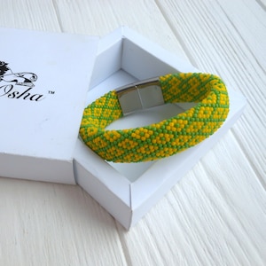 May include: A yellow and green beaded bracelet with a magnetic clasp. The bracelet is in a white box with the text "ifa-Osha" on the lid.