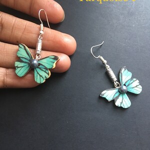 May include: A pair of turquoise butterfly earrings with silver hooks and black pearl accents. The earrings are displayed on a black surface. Turquoise 1.