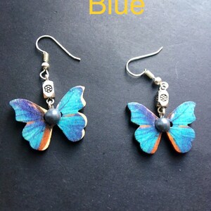 May include: A pair of blue butterfly earrings with silver accents. The butterflies are made of wood and have a blue and orange pattern. The earrings are hanging from silver hooks.