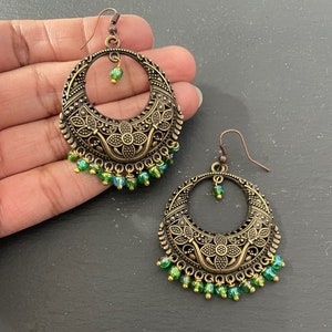 May include: A pair of gold-toned earrings with intricate floral designs and green glass beads dangling from the bottom.