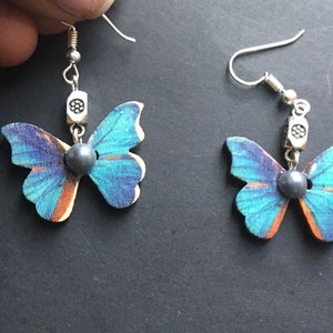 May include: A pair of butterfly earrings with blue and orange wings, silver accents, and a dark gray pearl in the center of each butterfly.