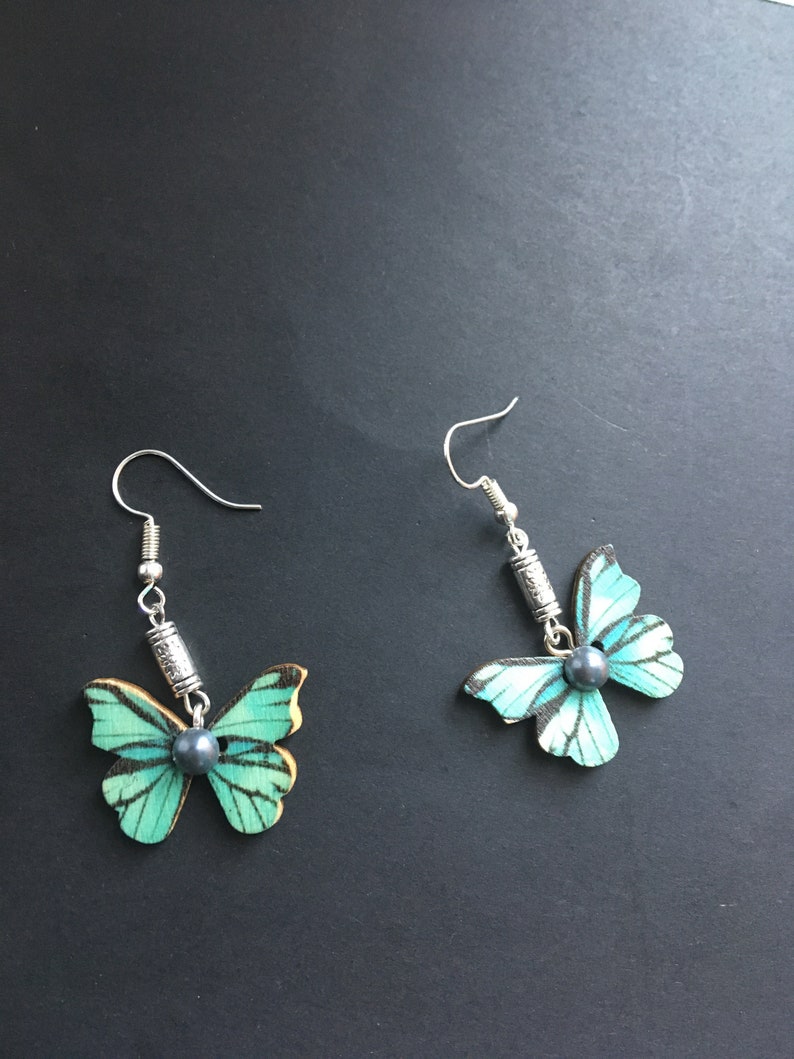 May include: A pair of silver butterfly earrings with a teal and black butterfly design and a dark gray pearl accent.
