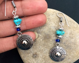May include: Silver dangle earrings with turquoise and blue beads and a silver circular charm with geometric designs.