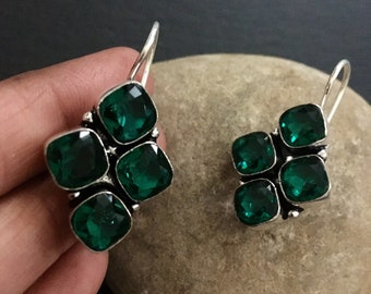 Può includere: Un paio di orecchini pendenti in argento con quattro pietre quadrate di colore verde smeraldo.