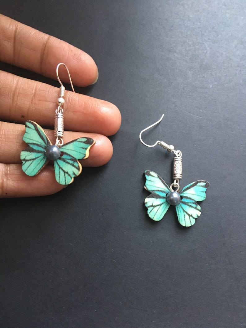 May include: A pair of silver butterfly earrings with a teal and white butterfly design and a black pearl accent.
