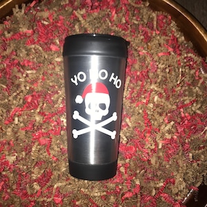 May include: A stainless steel travel mug with a black lid and a white design of a skull wearing a Santa hat and the text "Yo Ho Ho".