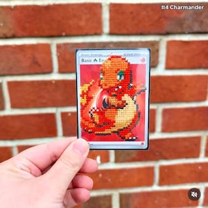May include: A rectangular trading card featuring a cross-stitched orange and yellow Charmander character on a red background. The card is labeled Basic Energy at the top and includes the text #4 Charmander in the upper right corner.