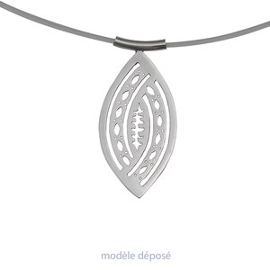 Peut inclure: Un collier avec un pendentif argenté en forme de feuille. Le pendentif présente un motif ajouré avec un motif central stylisé et est suspendu à un cordon gris. Le texte "modèle déposé" est en bas.