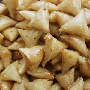May include: A close-up of a plate filled with golden brown, crispy fried pastries. The pastries are triangular in shape and appear to be filled with a savory or sweet filling.
