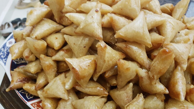 May include: A close-up of a plate filled with golden brown, crispy fried pastries. The pastries are triangular in shape and appear to be filled with a savory or sweet filling.