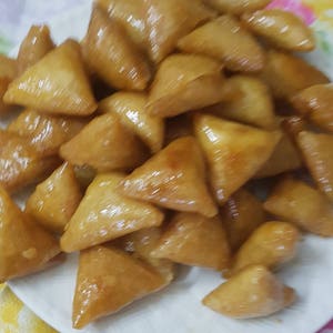 May include: A plate of golden brown, triangular shaped pastries covered in a shiny glaze.