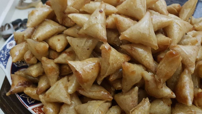 May include: A close-up of a large pile of golden brown, triangular pastries. The pastries are arranged in a random pattern and appear to be freshly made.