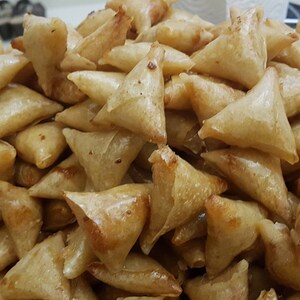May include: A close-up of a plate filled with golden brown, crispy fried pastries. The pastries are triangular in shape and appear to be a type of samosa or empanada.