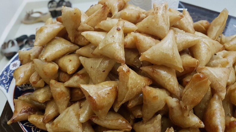 May include: A close-up of a plate filled with golden brown, crispy fried pastries. The pastries are triangular in shape and appear to be a type of samosa or empanada.