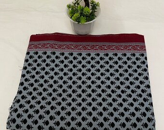 May include: A gray and black fabric with a repeating pattern of small black leaves. The fabric has a maroon border with a white and gray floral design.