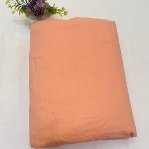 May include: A peach-colored fabric swatch. The fabric has a smooth, slightly textured surface.