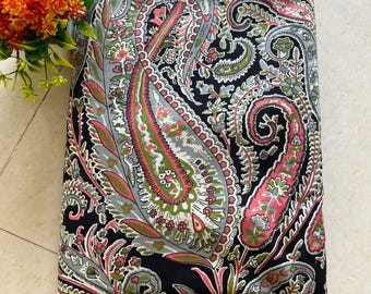 May include: A folded piece of fabric featuring a black background with a dense, multi-colored paisley pattern in shades of pink, light green, and grey. The intricate design includes swirling teardrop shapes and floral motifs.