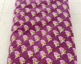 May include: A folded piece of fabric with a repeating pattern of pink flowers and green leaves on a burgundy background.