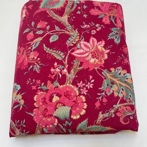 May include: A folded piece of fabric with a red background and a floral pattern in shades of pink, green, and brown.