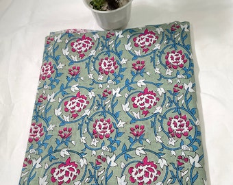 Op de afbeelding: Een groene stof met een bloemenprint met roze en blauwe bloemen op witte ranken. De stof is dubbelgevouwen en ligt op een wit oppervlak.
