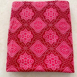 Könnte beinhalten: Roter Stoff mit einem weißen geometrischen Muster. Das Muster zeigt sich in sich wiederholenden Rauten und Blumenformen.