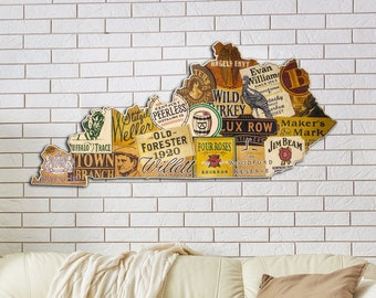 Può includere: Un ritaglio di legno dello stato del Kentucky, decorato con etichette vintage di vari marchi di bourbon del Kentucky, tra cui Wild Turkey, Maker's Mark, Jim Beam e Old Forester. Il ritaglio è esposto su un muro di mattoni bianchi.