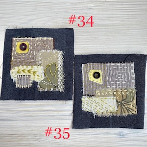 May include: Two square dark gray fabric patches featuring layered textile scraps in shades of brown, olive, and cream. Each patch includes visible hand-stitched embroidery, frayed edges, and a single dark button. The text #34 and #35 is visible.