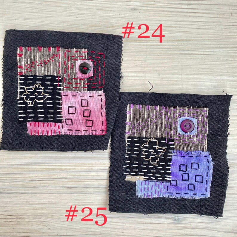 May include: Two square dark gray fabric patches featuring visible hand-stitched embroidery. Patch #24 displays pink and tan fabric squares with a black button. Patch #25 features purple and tan fabric squares with a purple button and white stitching.