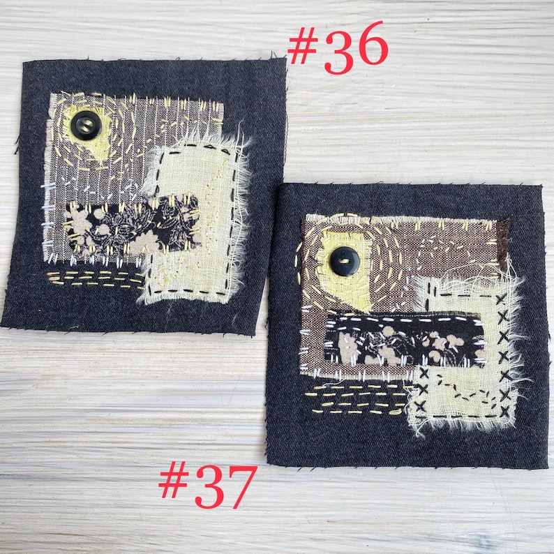 May include: Two square dark gray fabric patches labeled #36 and #37, featuring layered beige and black patterned textile scraps, visible white and yellow decorative running stitches, and a single black button sewn onto each piece.