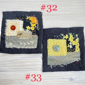 May include: Two square dark denim fabric patches labeled #32 and #33. Patch #32 features a white fabric square, a brown button, and yellow floral embroidery. Patch #33 features a yellow fabric square, a green button, and yellow floral embroidery.