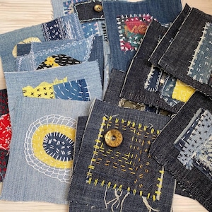 Può includere: Una collezione di toppe in denim, ognuna decorata in modo unico con cuciture visibili in vari colori. Alcune toppe presentano ricami decorativi, bottoni e dettagli in tessuto, mostrando un'estetica artigianale. Le toppe variano per dimensioni e forma.