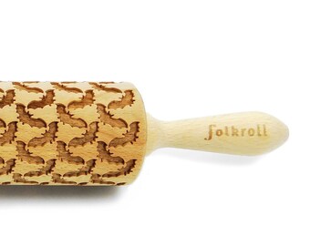 May include: A wooden rolling pin with a pattern of bats engraved on the surface. The rolling pin has a wooden handle with the word "Folkroll" engraved on it.