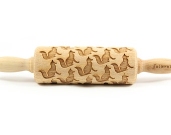 May include: A wooden rolling pin with a pattern of squirrels engraved on the surface. The rolling pin is made by the company "Folkroll".