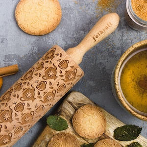 May include: A wooden rolling pin with a teacup and teapot design. The rolling pin is engraved with the word "folkroll".