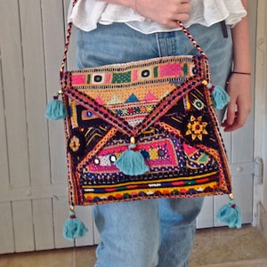 Può includere: Una borsa a tracolla colorata e ricamata con un cinturino lungo e nappe. La borsa è realizzata in tessuto patchwork e presenta una varietà di colori, tra cui rosso, blu, verde, giallo e rosa.