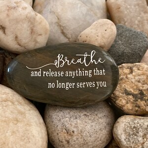 May include: A dark gray stone with the words "Breathe and release anything that no longer serves you" engraved in white.