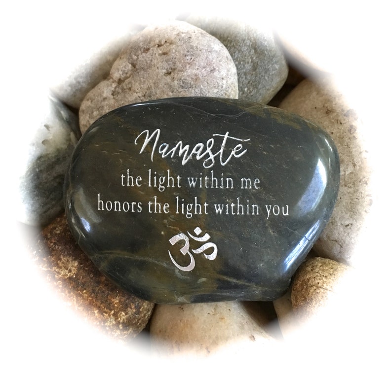 Op de afbeelding: Een donkergrijze steen met de woorden "Namaste the light within me honors the light within you" en het Om-symbool gegraveerd in zilver.