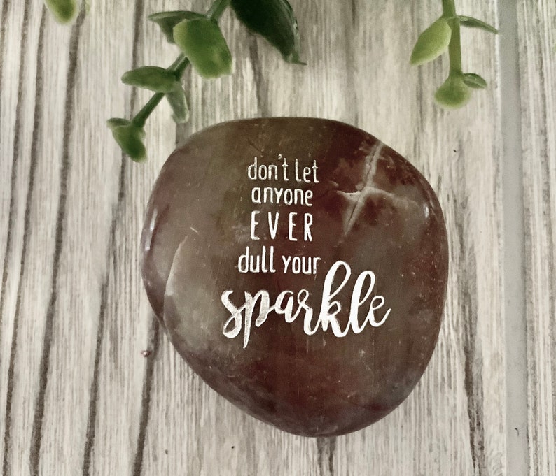 May include: A brown and white stone with the text "don't let anyone EVER dull your sparkle" engraved on it.