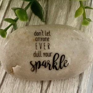 May include: A gray stone with the text "don't let anyone EVER dull your sparkle" written on it.