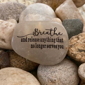 May include: A smooth, gray stone with the words "Breathe and release anything that no longer serves you" engraved on it.