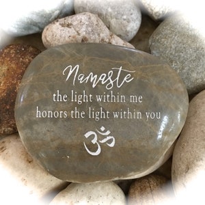 May include: A gray stone with the words "Namaste the light within me honors the light within you" and the symbol "Om" engraved on it.
