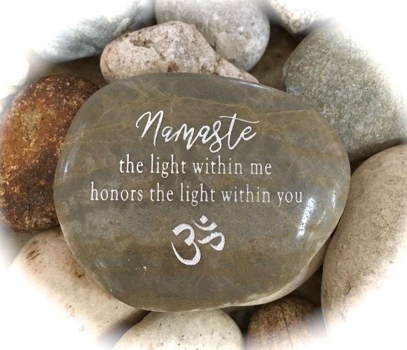 Op de afbeelding: Een grijze steen met de woorden "Namaste the light within me honors the light within you" en het symbool "Om" erop gegraveerd.