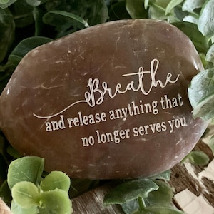 May include: A brown stone with the words "Breathe and release anything that no longer serves you" engraved on it.