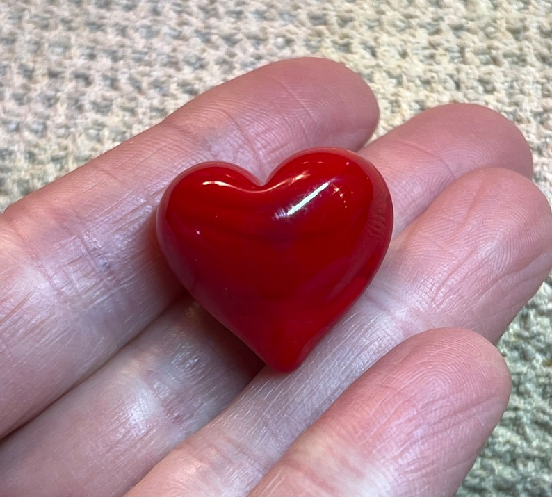 May include: A small, red heart-shaped glass paperweight. The heart is smooth and shiny.