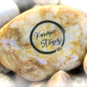 May include: A close-up of a light brown, round, smooth stone with a black circle and the text "Karmic Stones" inside the circle.