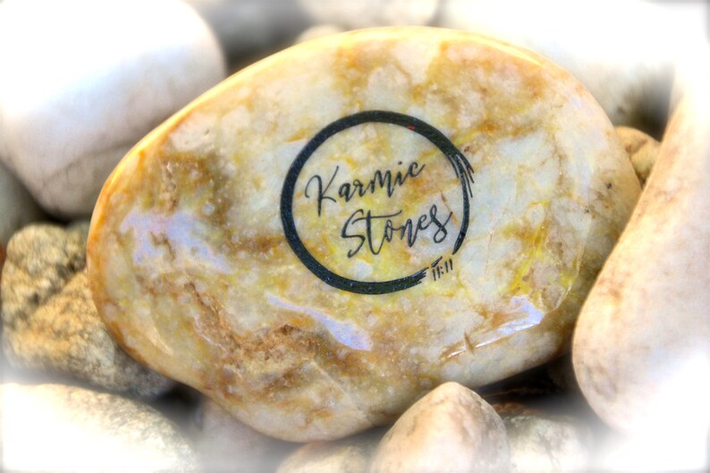 May include: A close-up of a light brown, round, smooth stone with a black circle and the text "Karmic Stones" inside the circle.